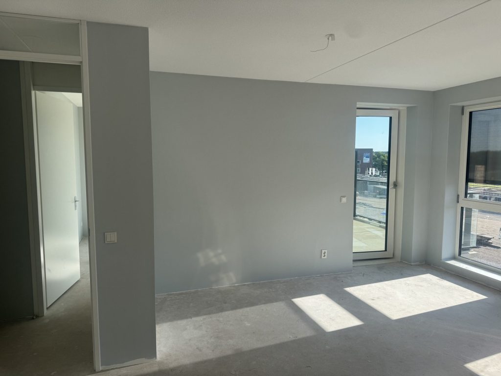 Lichtgrijze wanden in een nieuw appartement met een balkondeur en zon op de betonvloer