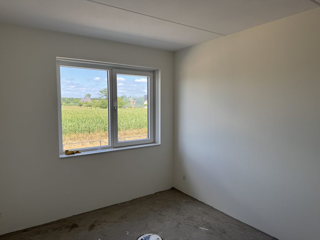 Lege kamer met strakke lichte wanden en een raam met uitzicht op een maisveld