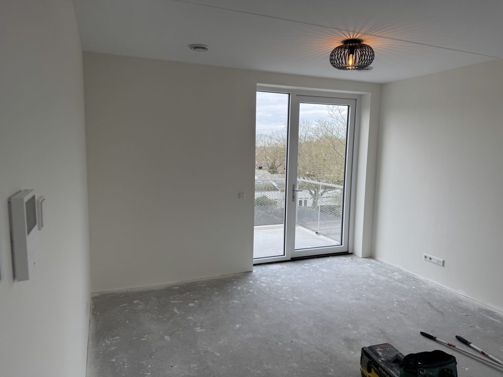 Lege kamer in een nieuw appartement met witte wanden, een hanglamp en een deur naar het balkon
